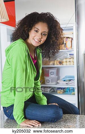 Woman sitting on a kitchen counter in front of a refrigerator View Large Photo Image Stock Image - Woman sitting on a kitchen counter in front of a refrigerator. Fotosearch