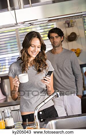 Woman text messaging with a man standing in the background View Large Photo Image Stock Image - Woman text messaging with a man standing in the background. Fotosearch