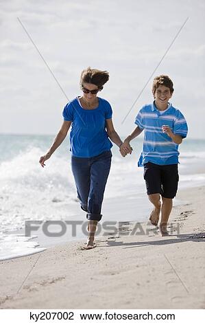 Stock Image - Woman running on the beach with her grandson. Fotosearch