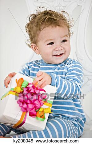 Baby boy holding a present in an armchair View Large Photo Image Stock Photography - Baby boy holding a present in an armchair. Fotosearch
