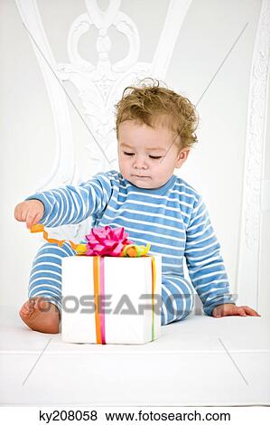 Baby boy playing with a present in an armchair View Large Photo Image Stock Photo - Baby boy playing with a present in an armchair. Fotosearch