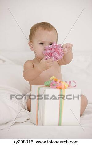 Stock Photograph - Baby girl playing with a bow on the bed. Fotosearch