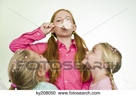Girl eating a lollipop with her two friends looking at her View Large Photo Image Stock Image - Girl eating a lollipop with her two friends looking at her. Fotosearch