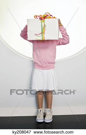 Girl holding a birthday present in front of her face View Large Photo Image Stock Photo - Girl holding a birthday present in front of her face. Fotosearch