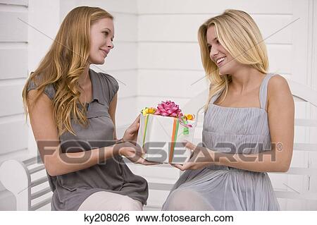 Woman giving a present to her friend View Large Photo Image Stock Photograph - Woman giving a present to her friend. Fotosearch