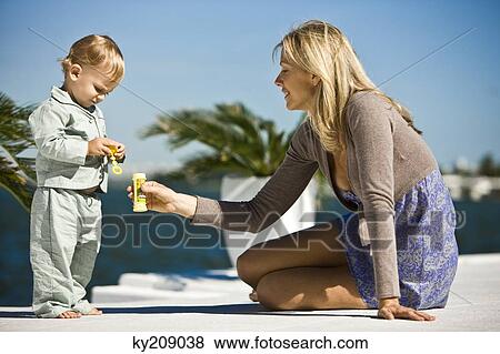 Stock Photo - Woman holding a soap bubble bottle in front of her son. Fotosearch