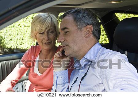 Stock Image - Man with his wife in a car and talking on a mobile phone. Fotosearch