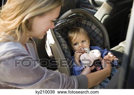 Stock Photo - Woman fastening her son on a baby seat in a car. Fotosearch