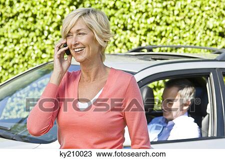 Woman talking on a mobile phone and her husband in a car in the background View Large Photo Image Stock Image - Woman talking on a mobile phone and her husband in a car in the background. Fotosearch