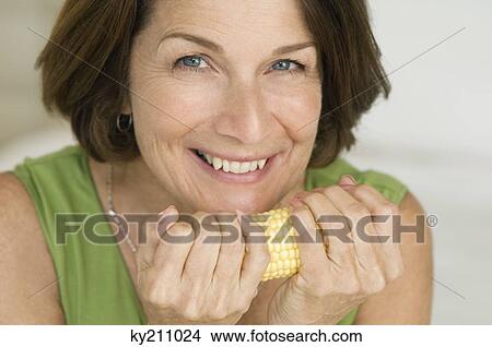 Picture - Woman holding a corn on cob and smiling. Fotosearch
