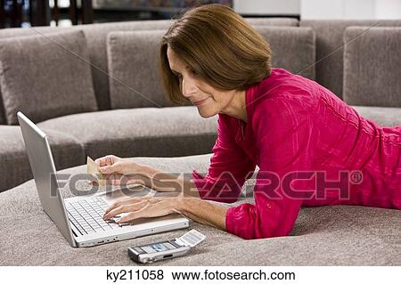 Woman holding a credit card and working on a laptop View Large Photo Image Stock Photo - Woman holding a credit card and working on a laptop. Fotosearch