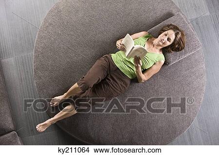 Woman lying on a round sofa and reading a book View Large Photo Image Picture - Woman lying on a round sofa and reading a book. Fotosearch
