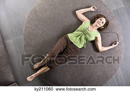 Woman lying on a round sofa and listening to headphones View Large Photo Image Stock Image - Woman lying on a round sofa and listening to headphones. Fotosearch