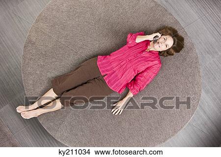 Picture - Woman lying on a round sofa and talking on a mobile phone. Fotosearch