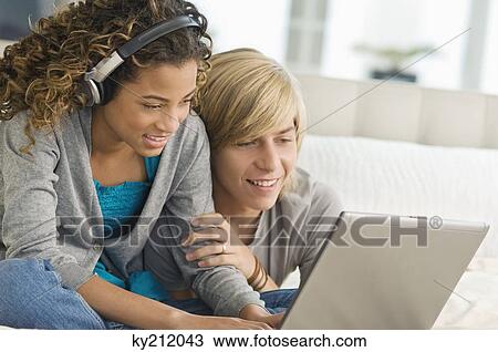 Girl listening to headphones and working on a laptop with a teenage boy beside her View Large Photo Image Stock Image - Girl listening to headphones and working on a laptop with a teenage boy beside her. Fotosearch