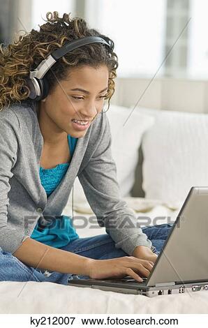 Stock Photo - Girl working on a laptop and listening to headphones. Fotosearch