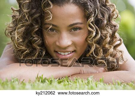Stock Image - Portrait of a girl lying on grass and smiling. Fotosearch