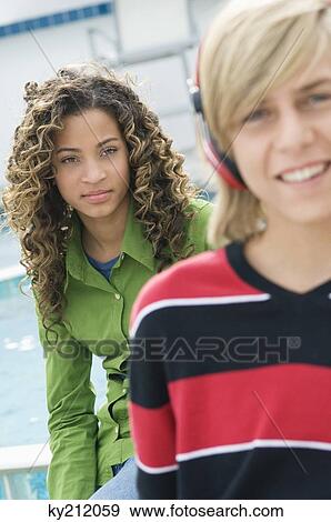 Teenage boy listening to music with headphones and a girl sitting behind him View Large Photo Image Stock Photo - Teenage boy listening to music with headphones and a girl sitting behind him. Fotosearch