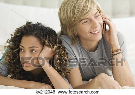 Stock Photo - Teenage boy talking on a mobile phone and lying beside a girl. Fotosearch