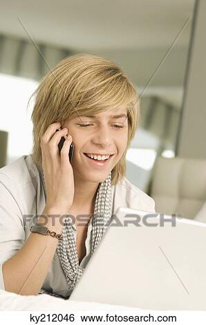 Stock Photograph - Teenage boy working on a laptop and talking on a mobile phone. Fotosearch