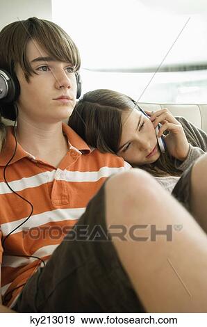 Boy listening to headphones and girl talking on a mobile phone View Large Photo Image Stock Photo - Boy listening to headphones and girl talking on a mobile phone. Fotosearch