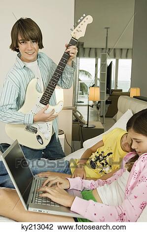 Stock Image - Boy playing a guitar and girl working on a laptop. Fotosearch