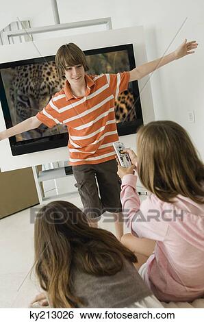 Girl holding a remote control and a boy standing in front of a television View Large Photo Image Stock Photograph - Girl holding a remote control and a boy standing in front of a television. Fotosearch