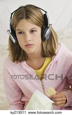 Stock Image - Girl listening to headphones and holding potato chips. Fotosearch