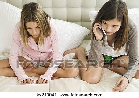 Girl talking on a mobile phone and her sister working on a laptop View Large Photo Image Stock Image - Girl talking on a mobile phone and her sister working on a laptop. Fotosearch