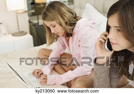Girl talking on a mobile phone and her sister working on a laptop View Large Photo Image Stock Image - Girl talking on a mobile phone and her sister working on a laptop. Fotosearch