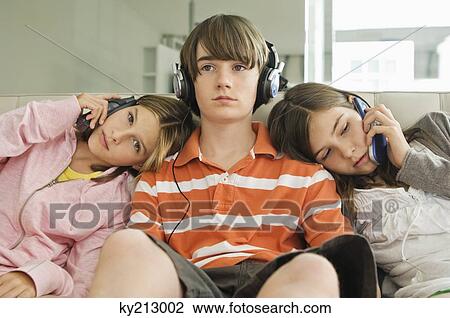 Two girls talking on mobile phones with a boy listening to headphones View Large Photo Image Stock Image - Two girls talking on mobile phones with a boy listening to headphones. Fotosearch