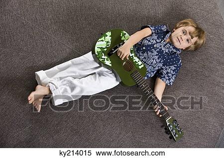 Boy lying on a round table and playing a guitar View Large Photo Image Stock Photography - Boy lying on a round table and playing a guitar. Fotosearch