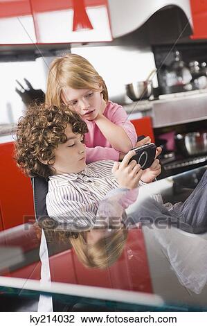 Boy playing a video game and his sister standing beside him View Large Photo Image Stock Image - Boy playing a video game and his sister standing beside him. Fotosearch