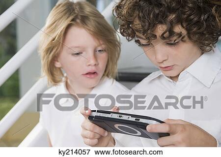 Boy playing a video game and his sister looking at it View Large Photo Image Stock Photo - Boy playing a video game and his sister looking at it. Fotosearch