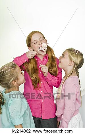 Girl eating a lollipop with her two friends standing beside her View Large Photo Image Stock Image - Girl eating a lollipop with her two friends standing beside her. Fotosearch