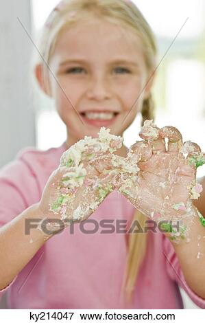 Stock Photo - Portrait of a girl showing her messy hand covered with cake icing. Fotosearch