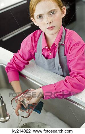 Stock Image - Portrait of a girl washing a measuring jug at a sink. Fotosearch