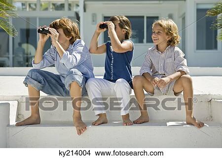 Two children looking through binoculars with their friend sitting beside them View Large Photo Image Picture - Two children looking through binoculars with their friend sitting beside them. Fotosearch