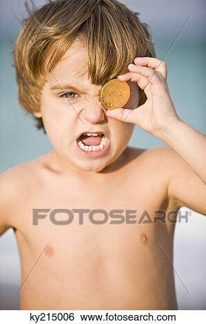 Stock Photograph - Portrait of a boy holding a coin in front of his eye. Fotosearch