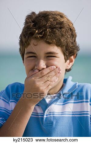 Stock Image - Portrait of a boy smiling with his mouth covered. Fotosearch