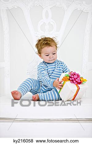 Baby boy playing with a present in an armchair View Large Photo Image Stock Photo - Baby boy playing with a present in an armchair. Fotosearch