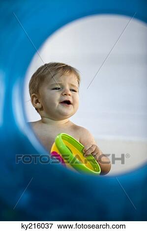 Stock Photo - Baby boy playing with a toy viewed through an inflatable ring. Fotosearch