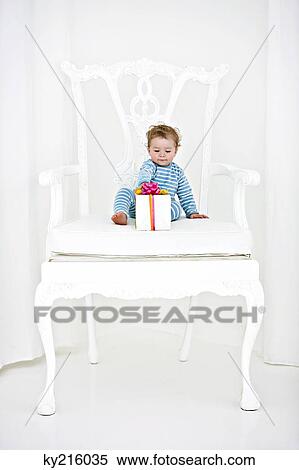 Baby boy sitting in an armchair with a gift View Large Photo Image Stock Photography - Baby boy sitting in an armchair with a gift. Fotosearch