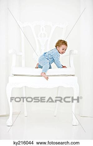Baby boy trying to get down from an armchair View Large Photo Image Picture - Baby boy trying to get down from an armchair. Fotosearch