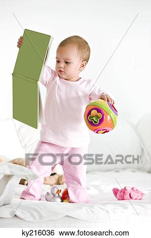 Baby girl playing with a picture book and a toy View Large Photo Image Stock Photograph - Baby girl playing with a picture book and a toy. Fotosearch