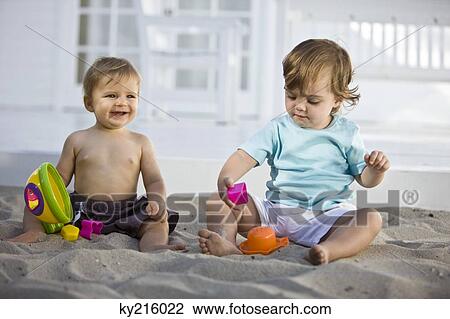 Two babies playing with toys in sand View Large Photo Image Stock Image - Two babies playing with toys in sand. Fotosearch
