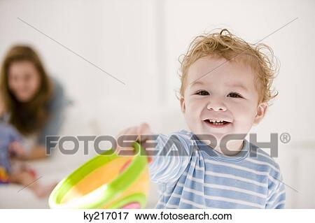 Boy holding a toy with his mother and sister in the background View Large Photo Image Stock Photo - Boy holding a toy with his mother and sister in the background. Fotosearch