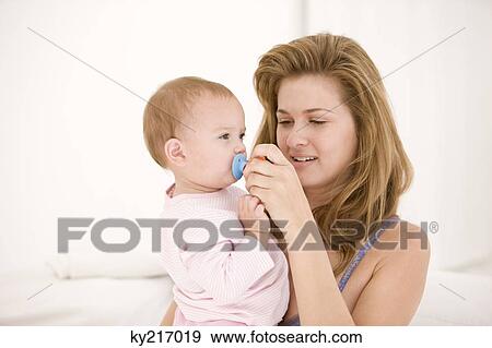 Stock Photo - Woman holding a pacifier on her daughter's mouth. Fotosearch