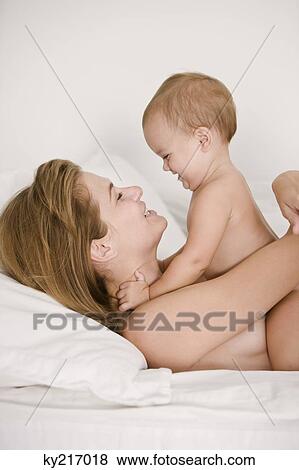 Woman lying on the bed and playing with her daughter View Large Photo Image Stock Photo - Woman lying on the bed and playing with her daughter. Fotosearch