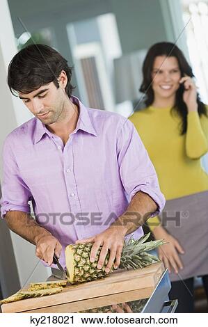 Man cutting a pineapple and a woman talking on a mobile phone behind him View Large Photo Image Stock Image - Man cutting a pineapple and a woman talking on a mobile phone behind him. Fotosearch
